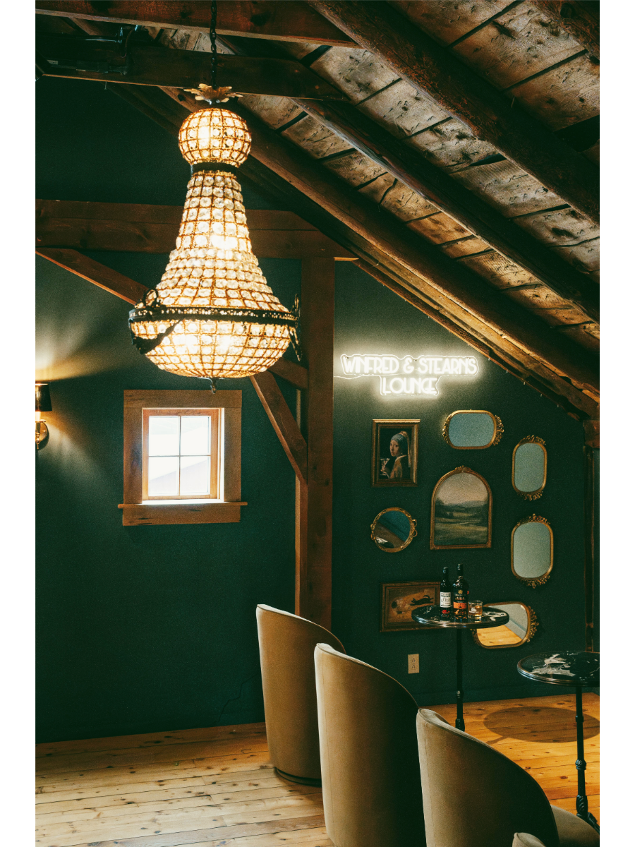 Cozy speakeasy lounge with chandelier, mirrors, and seating.