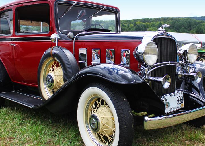 Vintage red and black car on grass with whitewall tires.