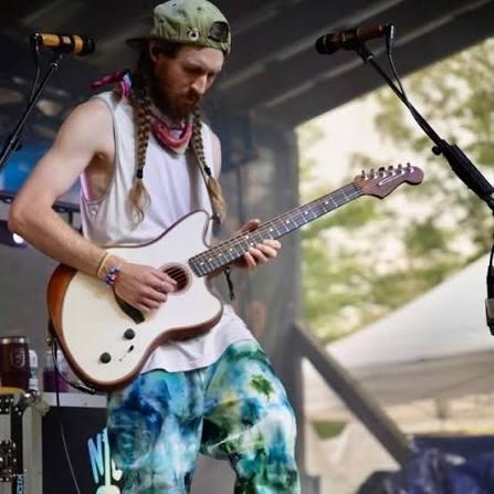 Man playing electric guitar on stage in casual attire.