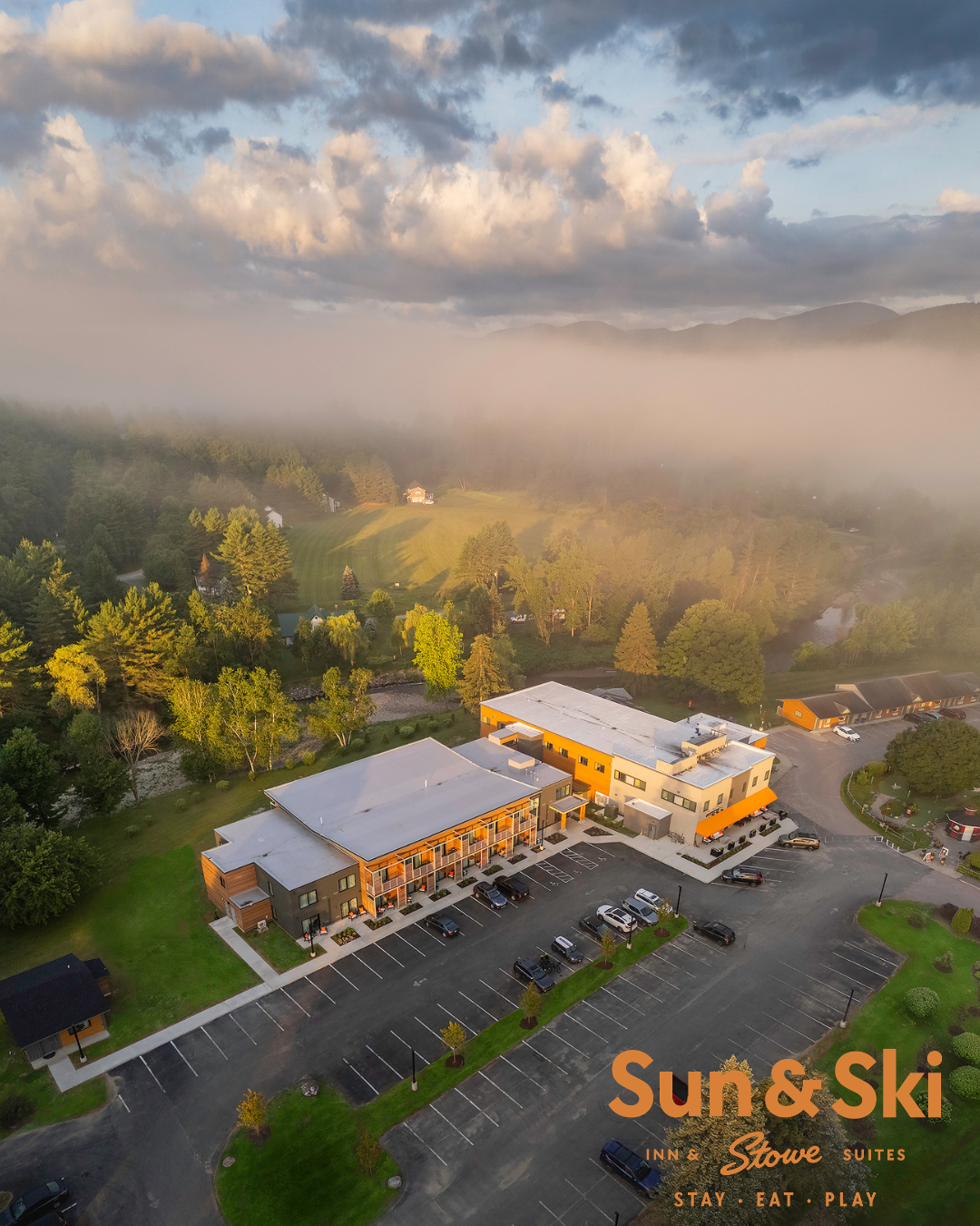 Aerial view of resort buildings surrounded by trees and mist.