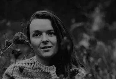 Black and white photo of a woman among wildflowers, wearing a patterned sweater.