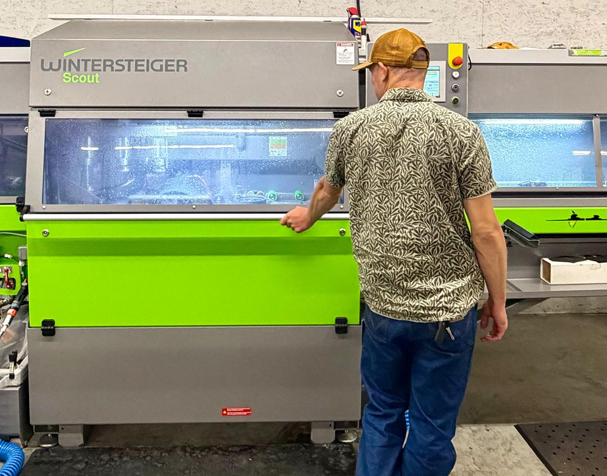 A man operates a large green and gray machine in an industrial setting.