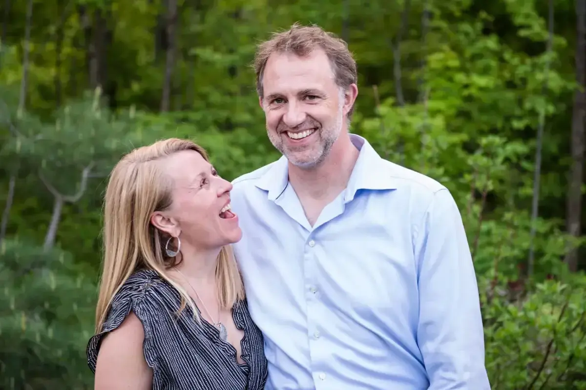 Smiling couple outdoors, surrounded by green foliage.