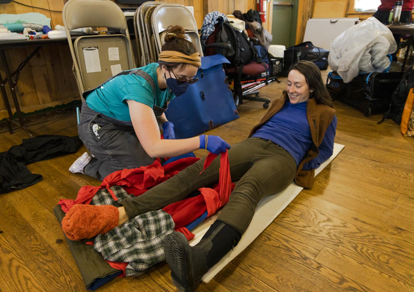 Woman administering first aid to a person lying on a mat indoors.