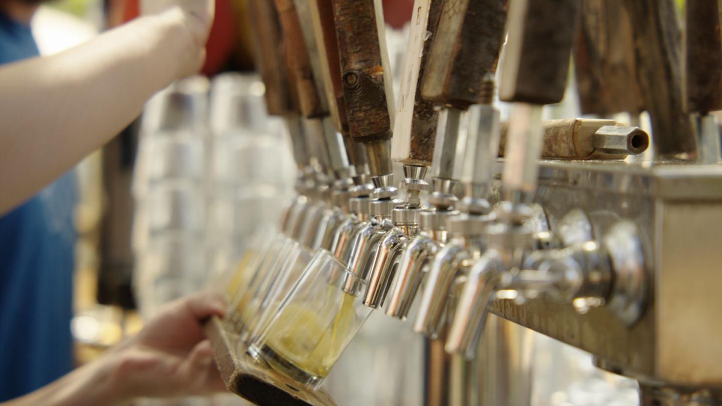 Bartender pouring beer from a row of taps into a glass.