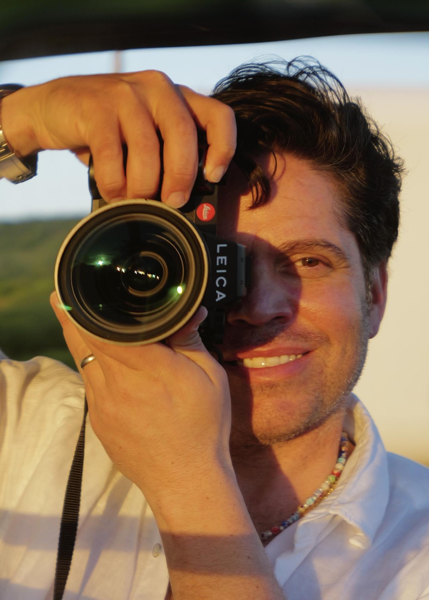 Smiling person holding a camera outdoors.