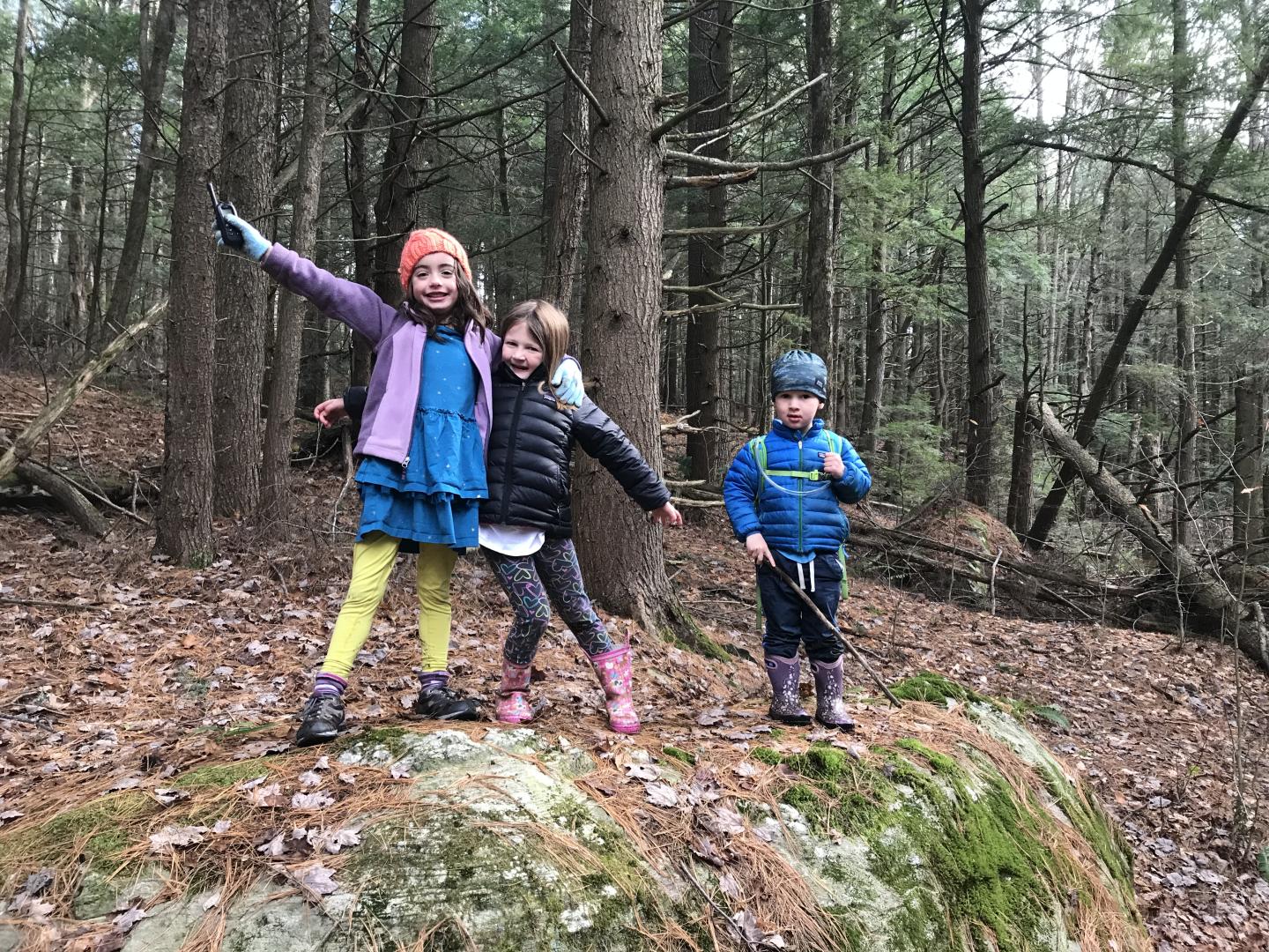Three children hiking and smiling in a wooded forest.