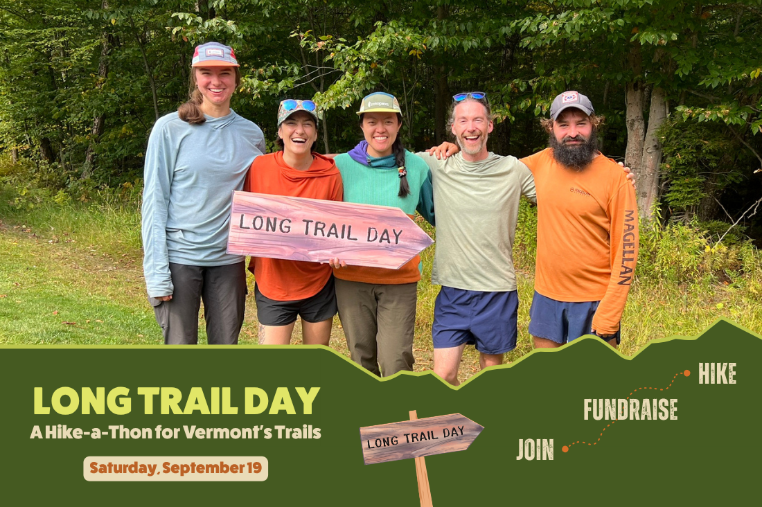 Four hikers hold a Long Trail Day sign on a wooded trail.