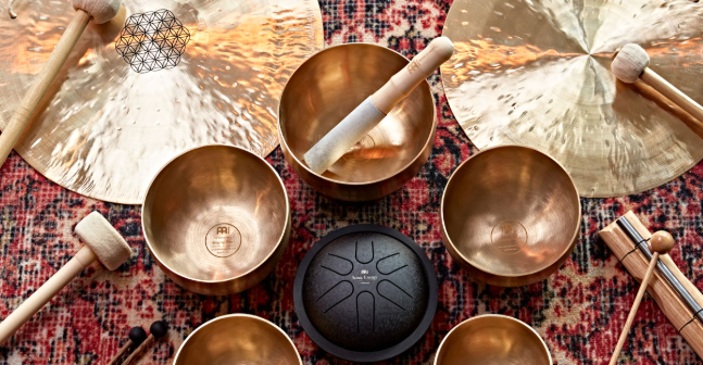 Singing bowls, cymbals, and drum on a patterned rug.