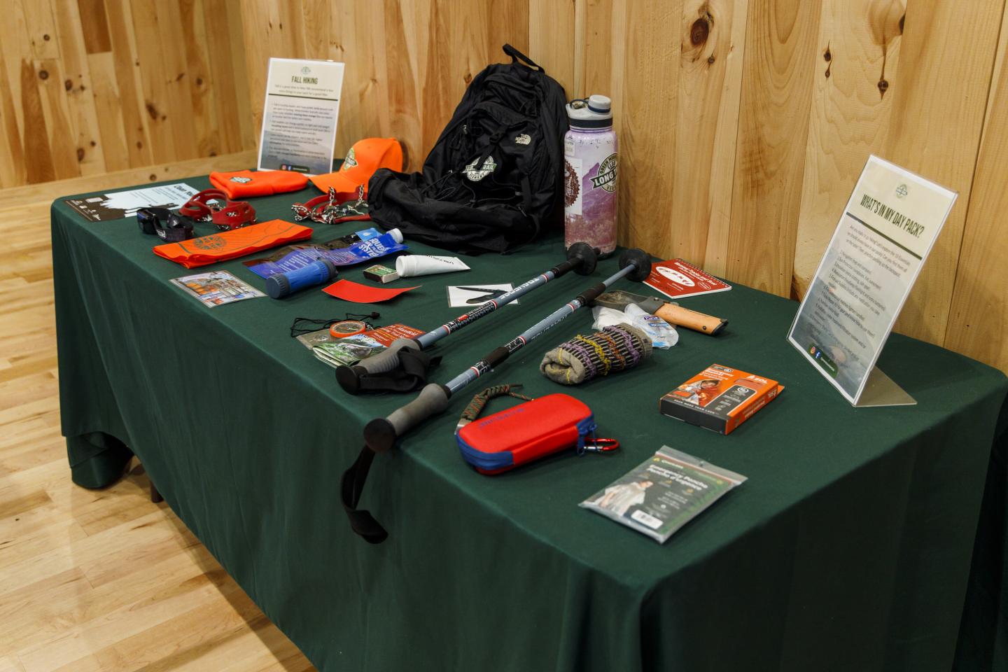 Table display of hiking ten essentials, including first aid kit, water, snacks, headlamps, clothing layers, and more
