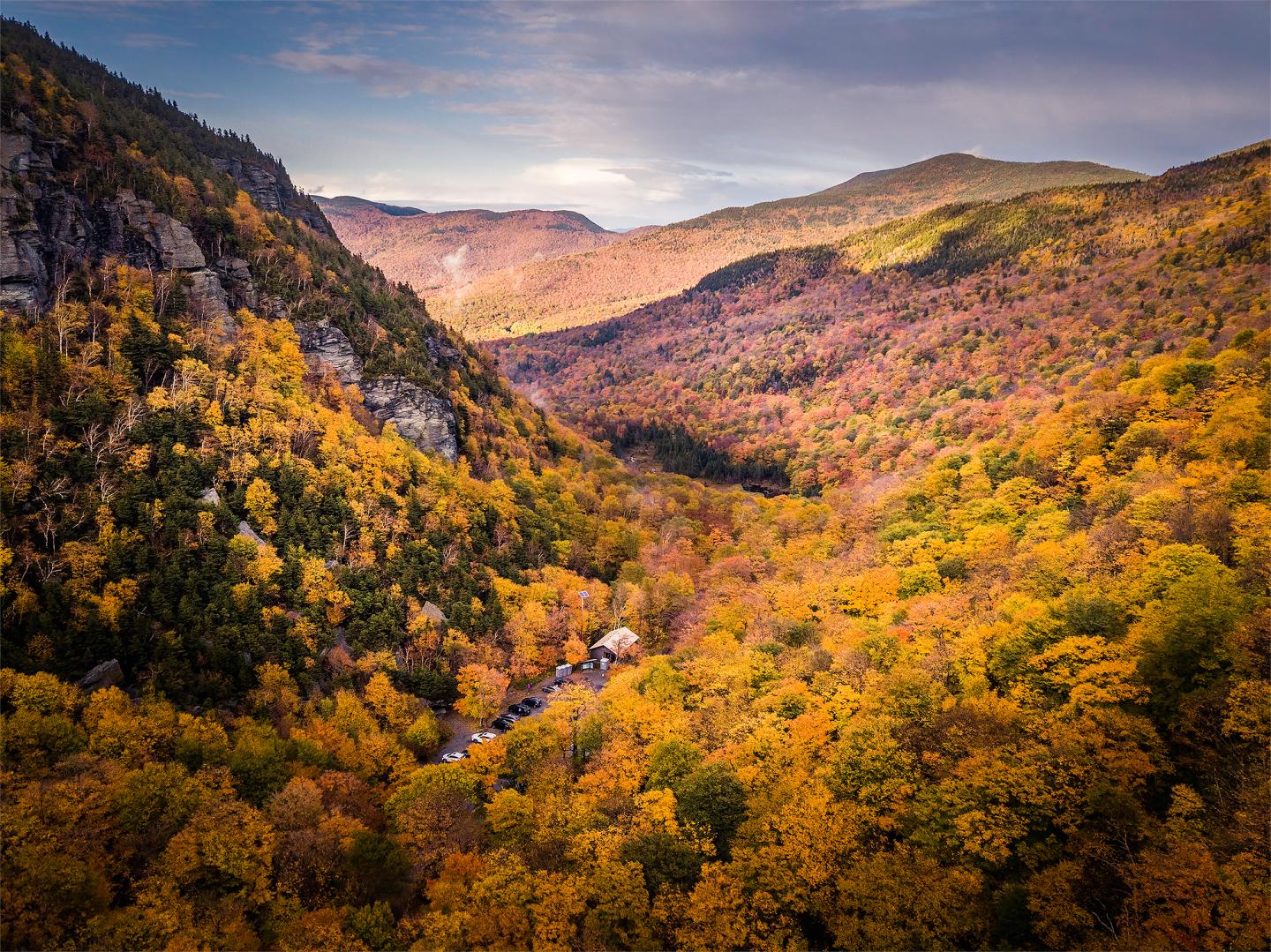 Autumn forest valley with rocky cliffs and colorful hills at sunset.