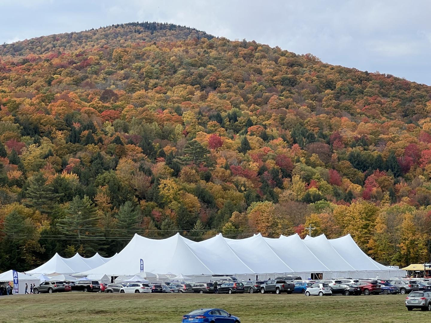 White event tents beneath a forested hillside in autumn colors
