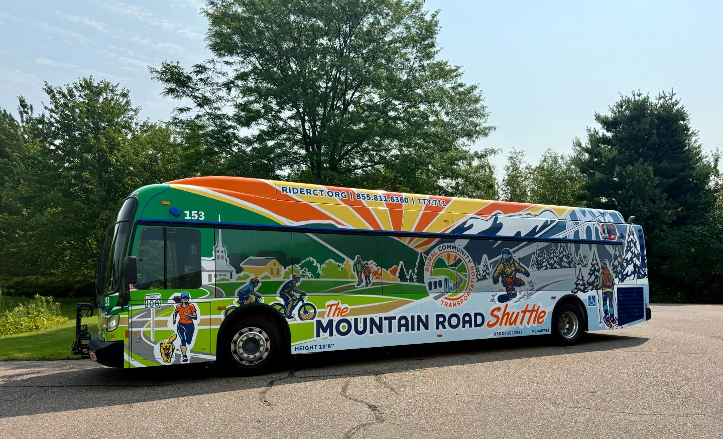 Colorful Mountain Road shuttle bus parked beside trees.
