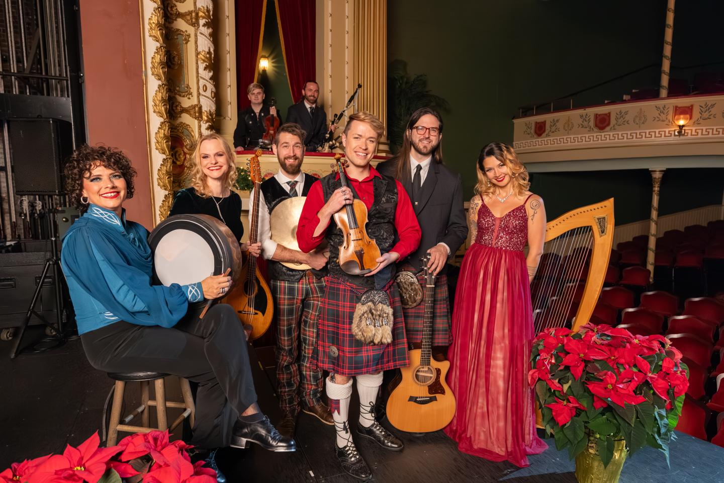 Musicians in festive attire pose with instruments on a theater stage.