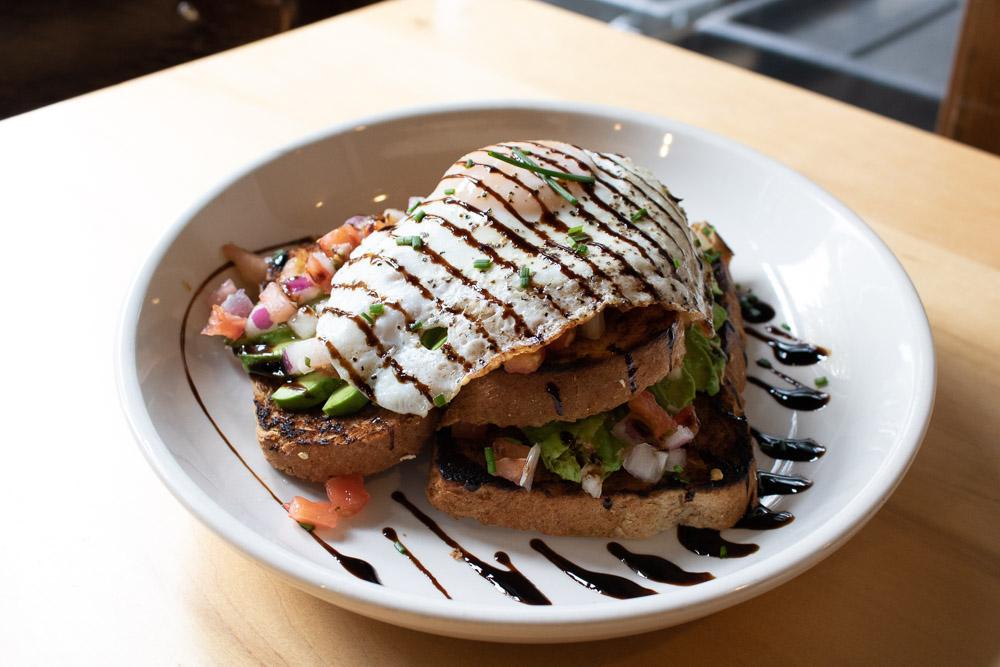 Grilled chicken sandwich with avocado, drizzled sauces, and fries on a white plate