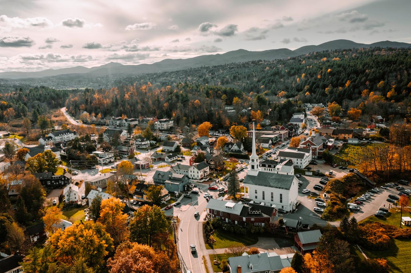 Aerial view of a small town among autumn trees and forested hills.