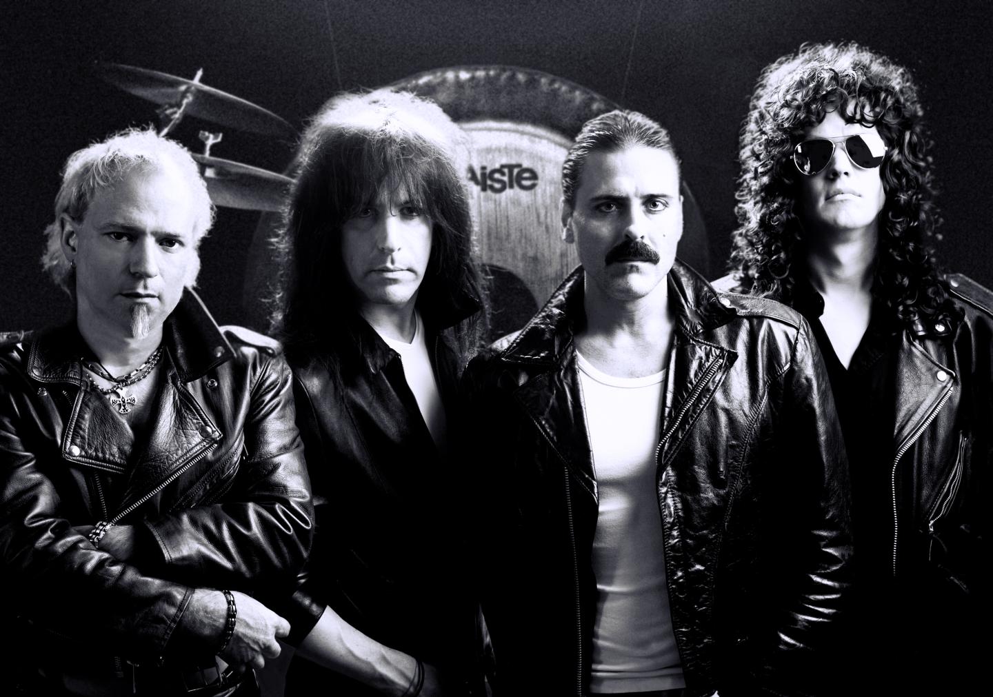 Black-and-white photo of four men in leather jackets posing against a dark background.