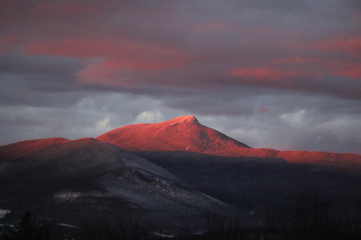 Sunset light illuminates a mountain peak beneath dramatic gray and red clouds.