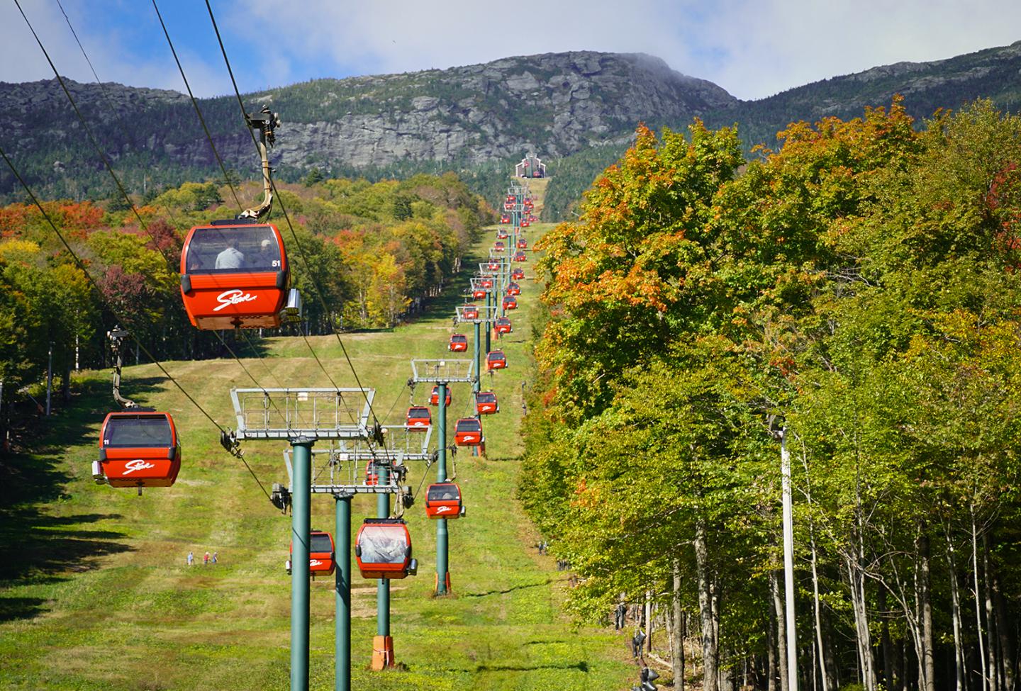 Red gondola lift cabins travel over a green valley in autumn.
