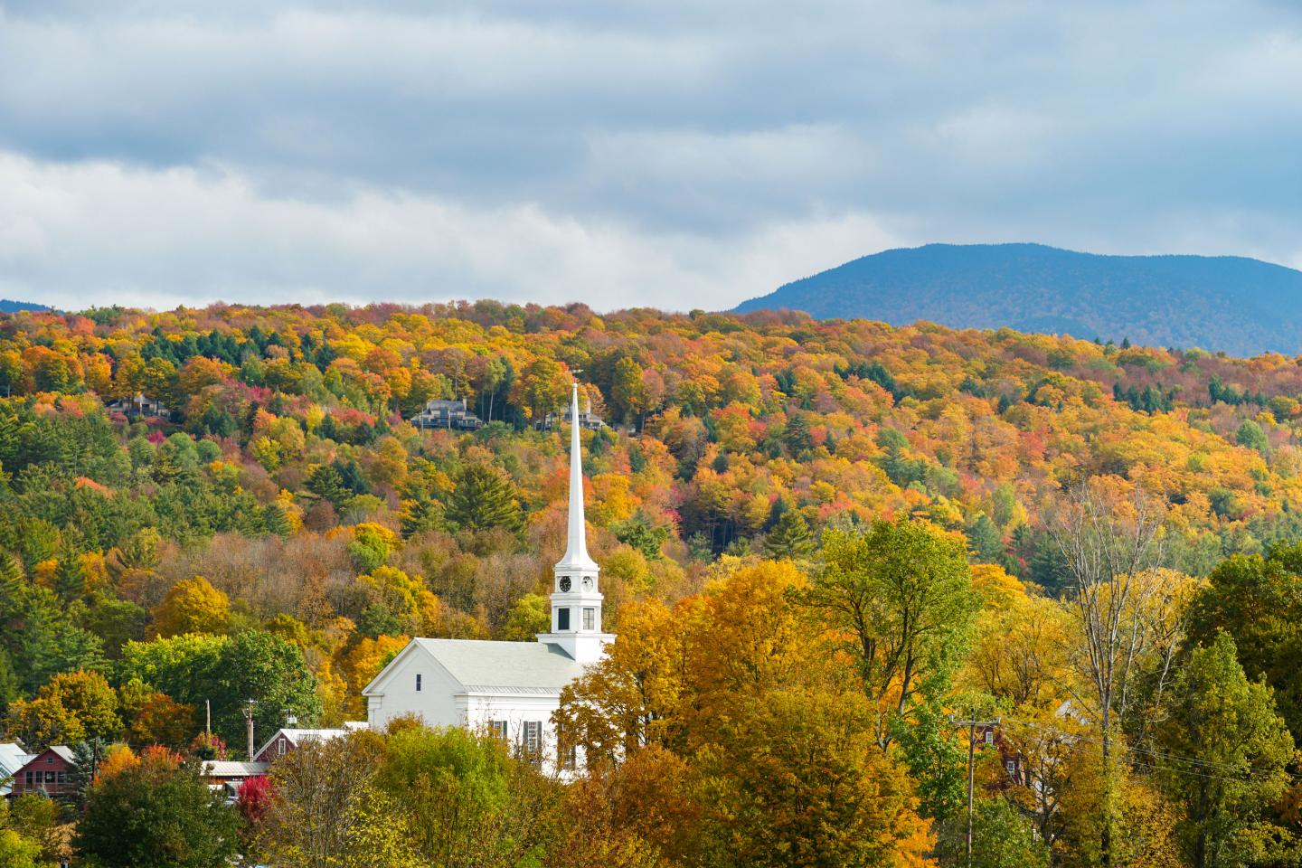 White church steeple amid autumn forest, with blue mountain in the distance.