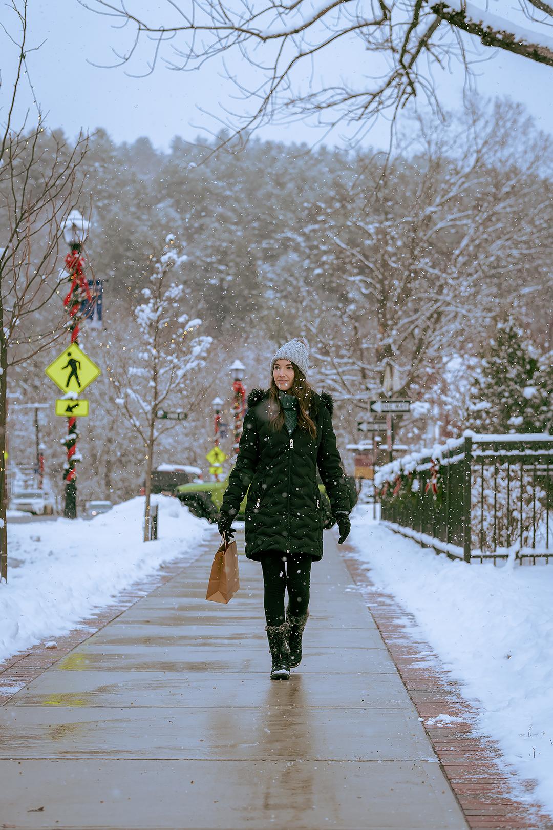 Woman walking on a snowy sidewalk beside a winter forest.