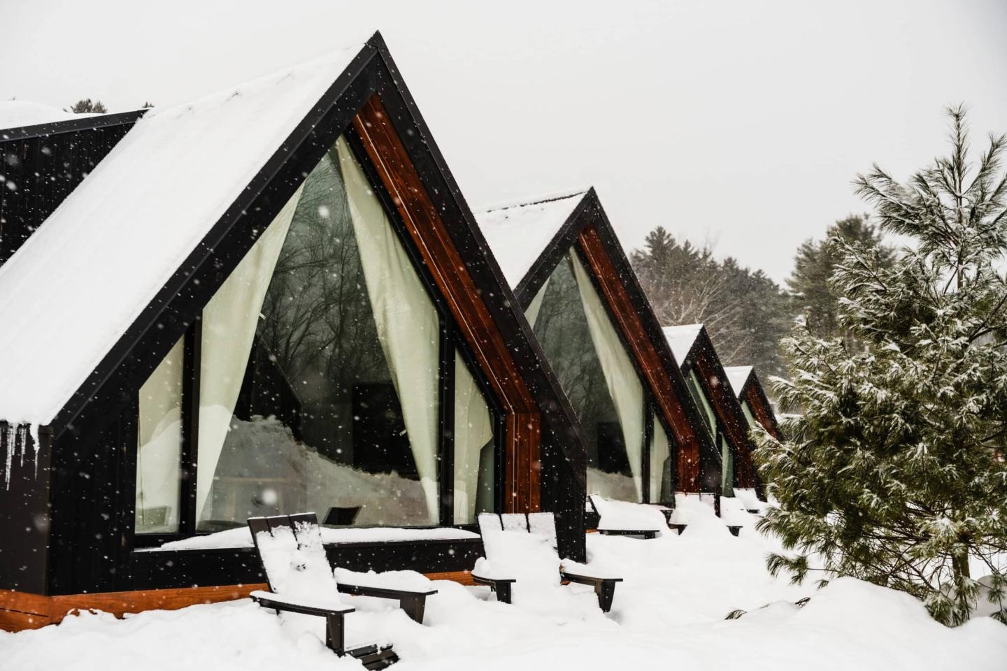 Snow-covered A-frame cabins in a winter forest.